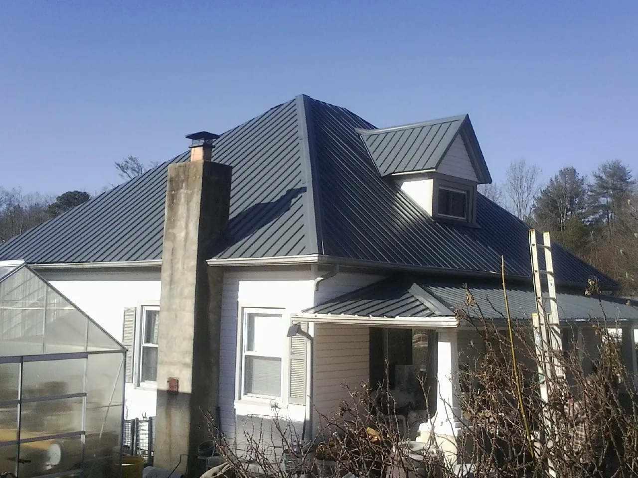 Dark blue standing seam metal roof on a white farmhouse with dormer — Slate & Tile Roof Repair by Roofing Brothers in Bell