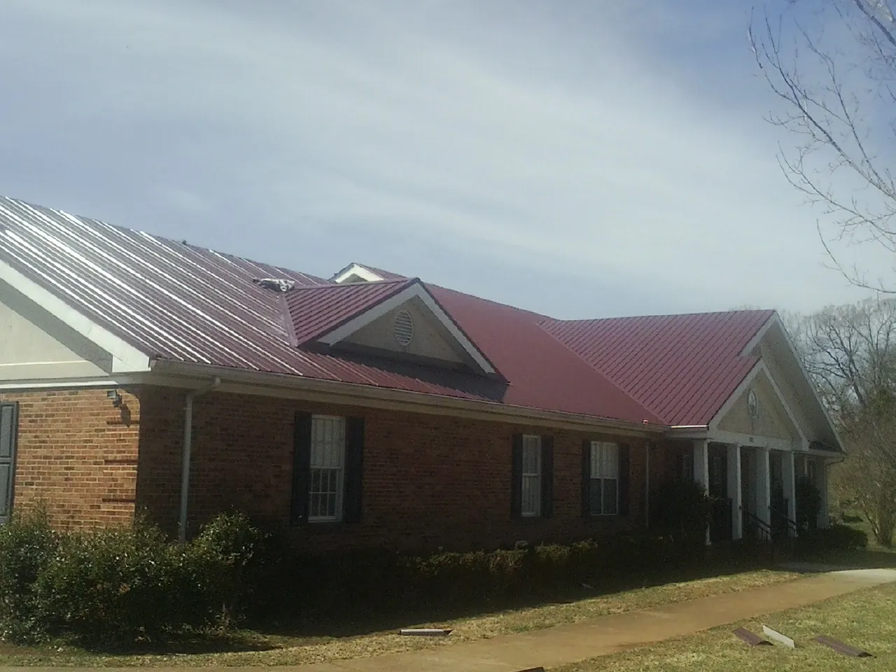 Red metal roof with gabled entries on a long brick building, from a Hail Damage Roof Repair job in Bell