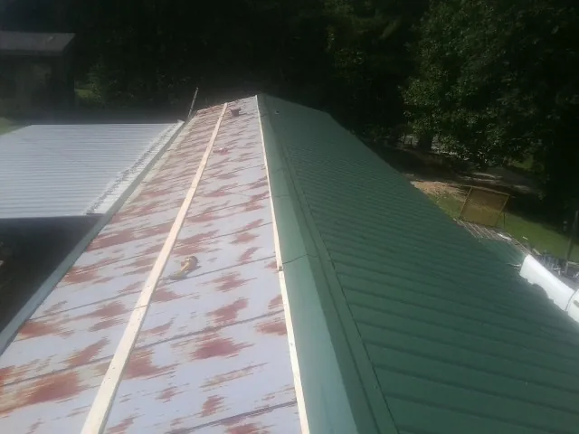 Old rusted panels beside newly installed green metal roofing — Wind Damage Roof Repair by Roofing Brothers in Bell